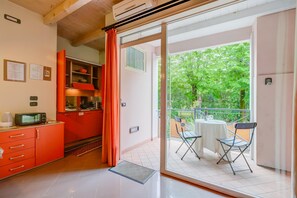 Una cocina con armarios rojos y un ventanal corredero que da a un balcón con mesa y sillas.