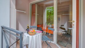 Un balcon avec une table dressée pour deux personnes, agrémentée d’une bouteille de vin, d’un panier de fruits et d’un verre.
