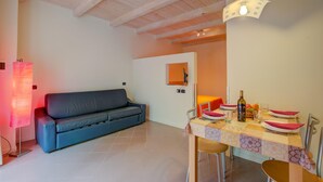 Un salon moderne avec un canapé bleu, une table à manger dressée avec des assiettes et une bouteille, et un plafond en bois.