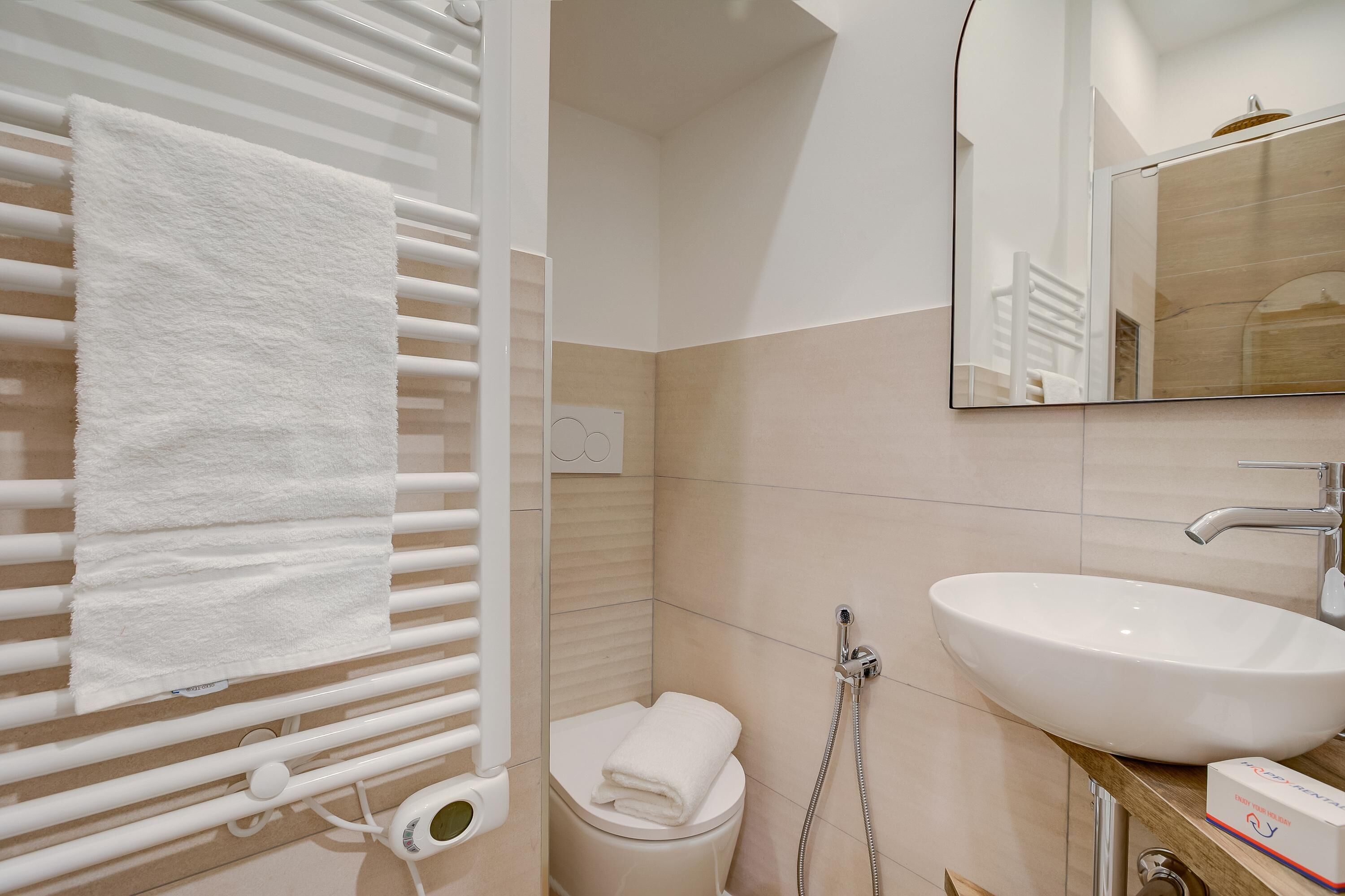 A bathroom with a white sink, a towel rack, a toilet, and a mirror.