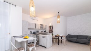 Una cocina moderna con armarios blancos, un comedor con mesa y sillas, y un sofá gris en la sala de estar.