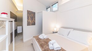 Habitación de hotel con cama, mesita de noche, toallero, armario y ventana.