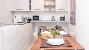 Una cocina moderna con armarios blancos, una mesa de comedor de madera dispuesta con platos, vasos y una botella.