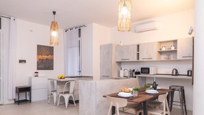 Una cocina moderna con una isla central, armarios blancos y un microondas. Hay una zona de comedor con una mesa y sillas de madera.