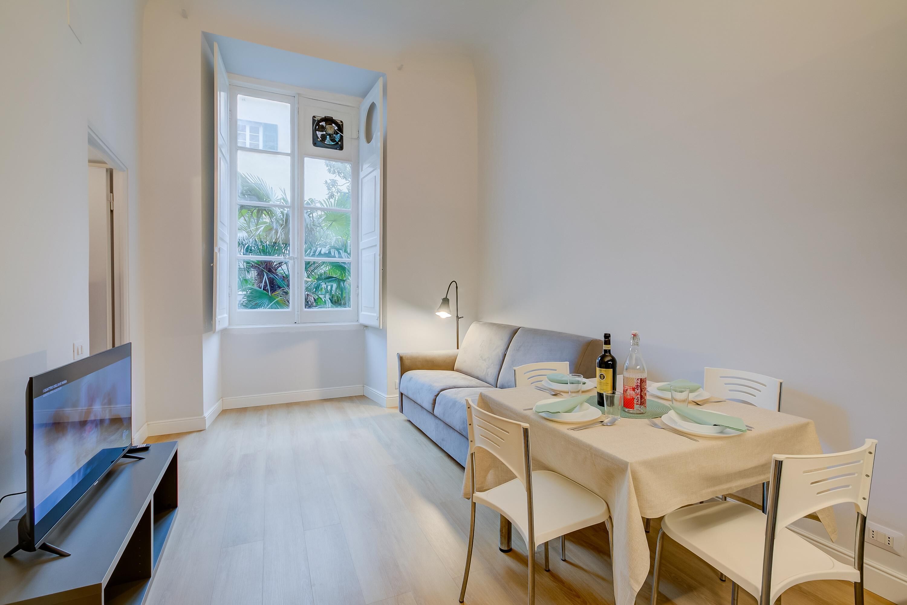 Un comedor moderno con una mesa preparada para dos personas, un sofá y un televisor sobre un mueble.