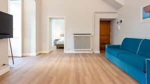 A spacious living room with a blue sofa, wooden flooring, a radiator, and a TV mounted on the wall. - Royal - Historic Center (Genoa)