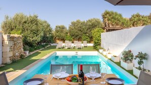 A dining table set for two with a bottle of wine, glasses, and a bowl of fruit. - Ta Patee Pool Farmhouse in Gozo (San Lawrenz)
