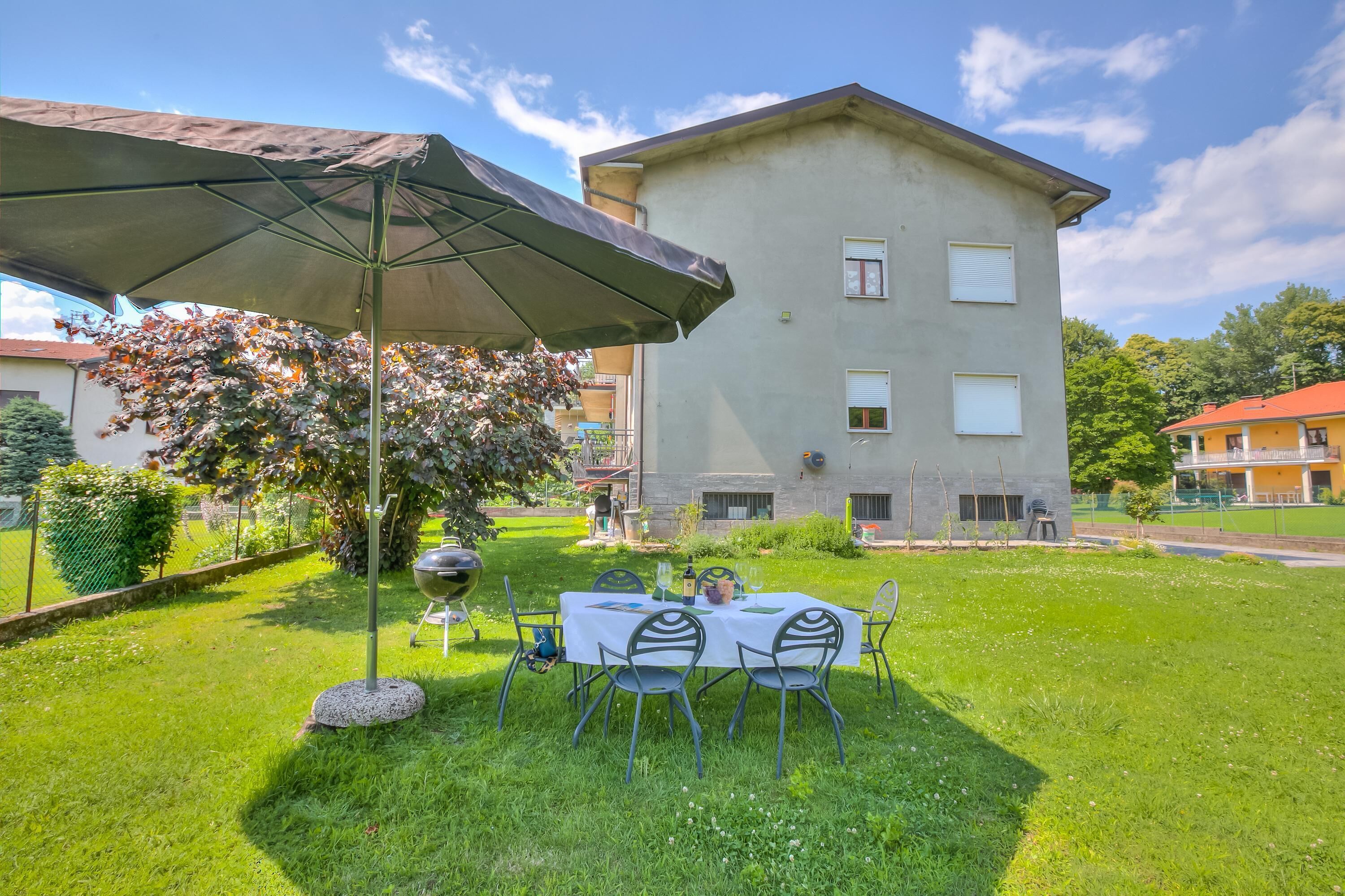 Un espace extérieur aménagé pour les repas, avec une table et des chaises, un barbecue et un grand parasol.