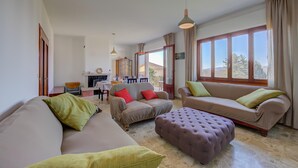 A spacious living room with a sofa, ottoman, and a dining area in the background.