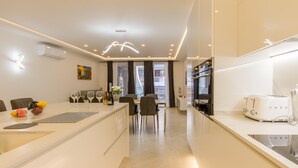 A modern kitchen with white cabinetry, a central island, and a dining area with chairs and a table. - Top Modern Prime Location 2mn to the sea (St. Paul's Bay)