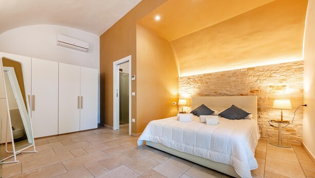 Une chambre avec un grand lit, une armoire blanche et un mur en pierre.