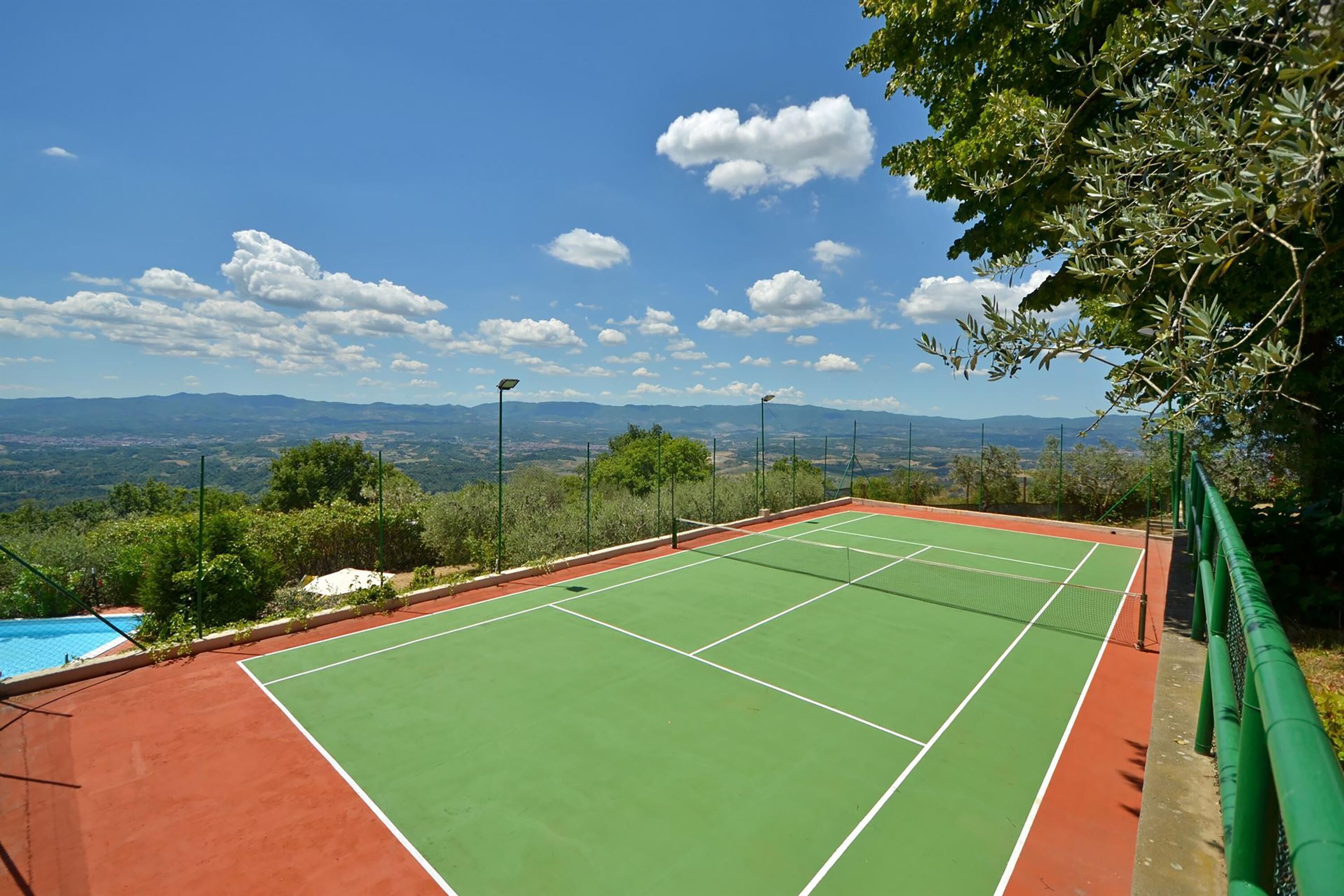 A tennis court with a clear view of mountains and a swimming pool in the background.