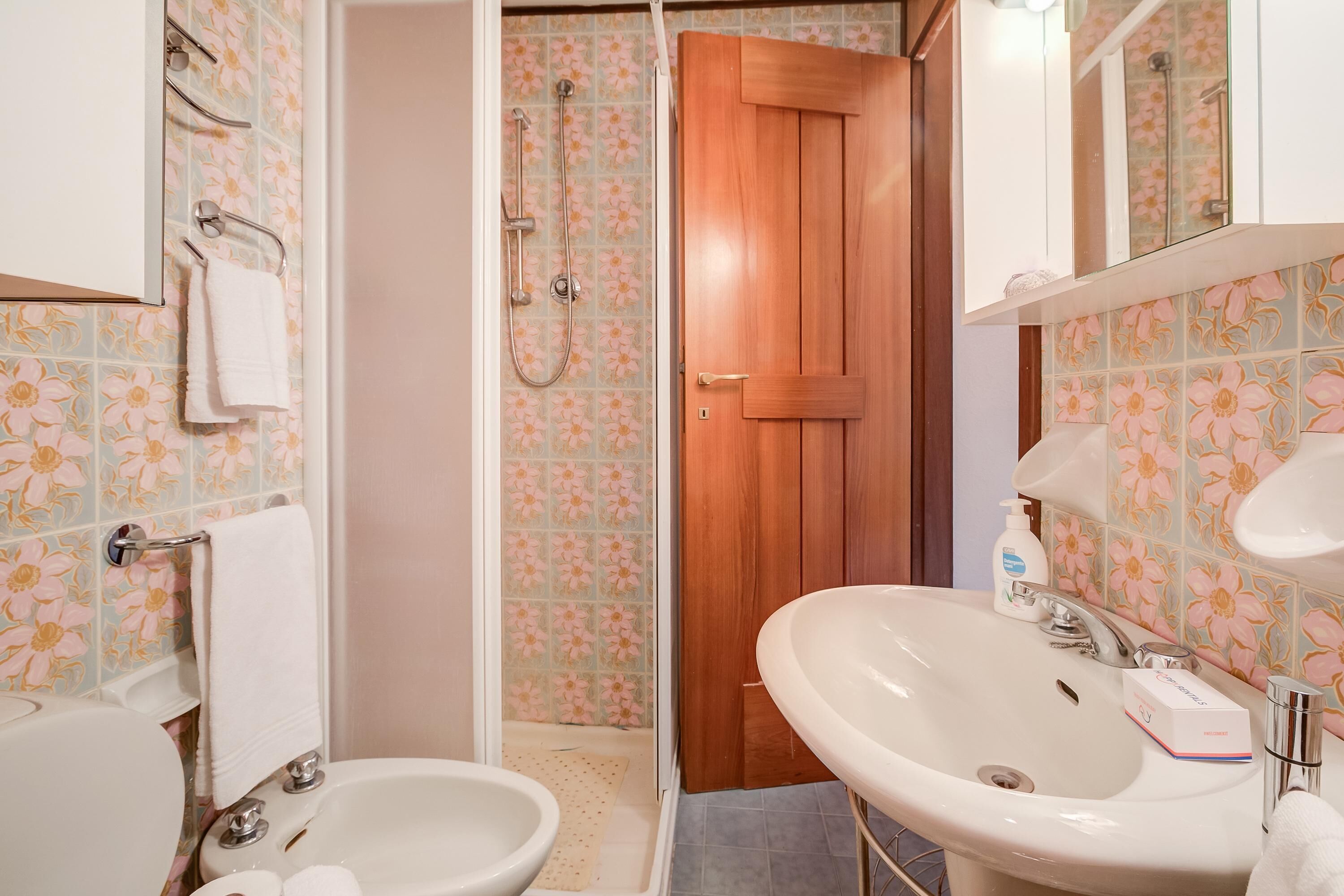 A bathroom with a wooden door, a white sink, and a bidet.
