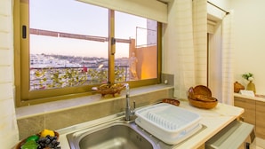 A kitchen with a large window, a sink, and a countertop with bowls and a fruit bowl. - Madonnina Sunny Townhouse in Kalkara (Kalkara)
