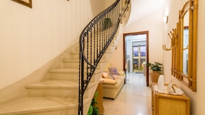 A staircase with a black railing leading to a landing area with a sofa and a mirror. - Madonnina Sunny Townhouse in Kalkara (Kalkara)