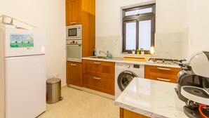 A modern kitchen with wooden cabinets, a built-in oven, microwave, and a window above the sink. - The Strand - Apartment By The Sea Sliema (Sliema)