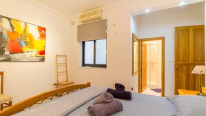 A hotel room with a bed, a window, a painting, and a door leading to another room. - The Strand - Apartment By The Sea Sliema (Sliema)