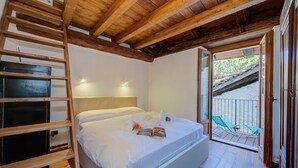 Ein Schlafzimmer mit Holzboden, einem Bett mit weißen Leinentüchern, einer Himmelsleiter und Blick auf einen Balkon mit Stühlen.