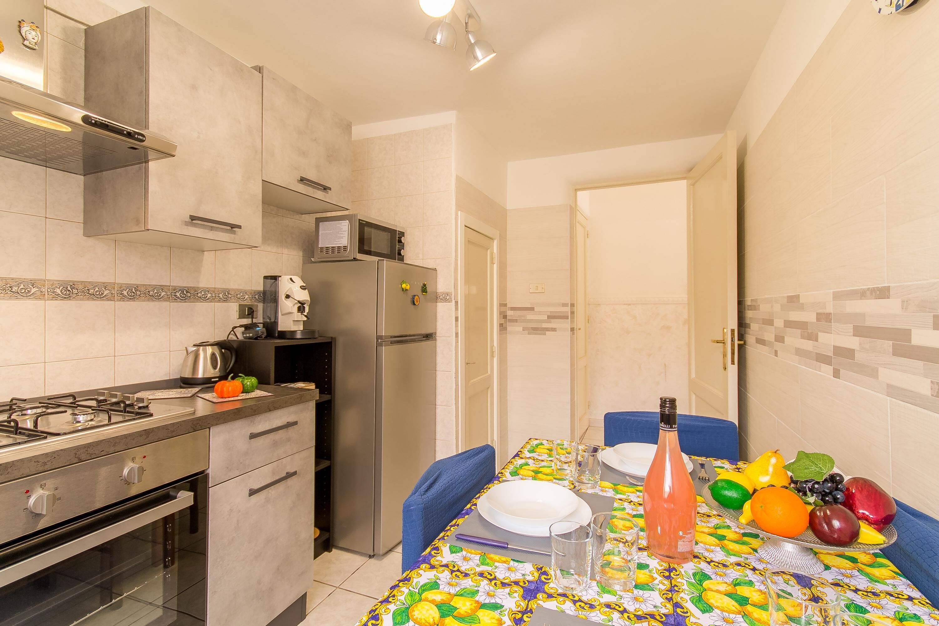 Une cuisine moderne équipée d’appareils électroménagers en acier inoxydable, un coin repas avec une table dressée pour deux personnes, et une porte donnant sur une autre pièce.