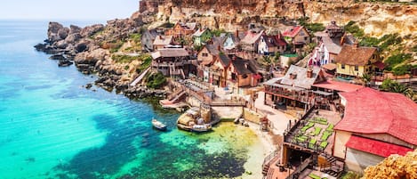 A coastal village with traditional architecture, a pier extending into the sea, and clear turquoise waters.