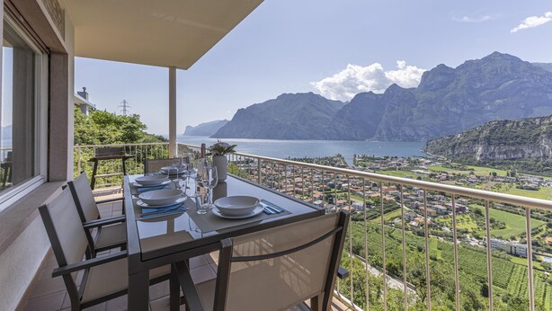 A balcony with a table set for dining, overlooking a mountainous landscape and a body of water. - Villa Panorama With Private Pool (Nago-Torbole)