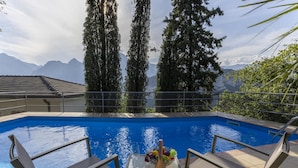 A poolside area with a glass table, two chairs, a bottle of champagne, and a fruit bowl. - Villa Panorama With Private Pool (Nago-Torbole)