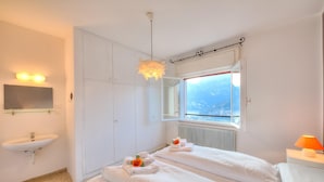 A hotel room with two beds, a bathroom with a sink, a mirror, and a window with a view of mountains. - Villa Panorama With Private Pool (Nago-Torbole)