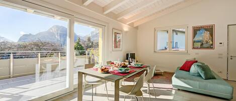 A spacious living area with a balcony, a dining table set with plates and glasses, and a green sofa.
