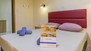 A hotel room with a bed, a nightstand, a wall-mounted light, and a sign for Happy Rentals. - Merill Pool and Sea Charming Apart 2 (Mellieha)