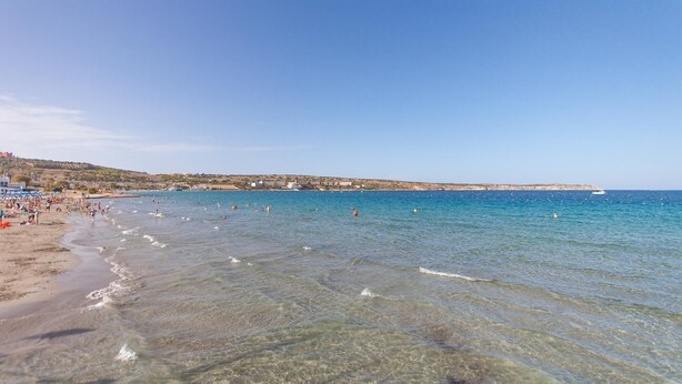 A beach with clear water, a sandy shore, and buildings in the background. - Merill Pool and Sea Charming Apart 2 (Mellieha)
