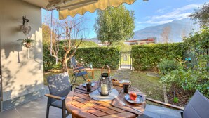 A patio with a table set for breakfast, outdoor seating, and a view of the garden and mountains. - The Peace Of The Lake (Arco)