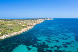 An aerial view of a coastal landscape with clear blue waters, rocky cliffs, and sparse vegetation. - Merill Pool and Sea Charming Apart 3 (Mellieha)