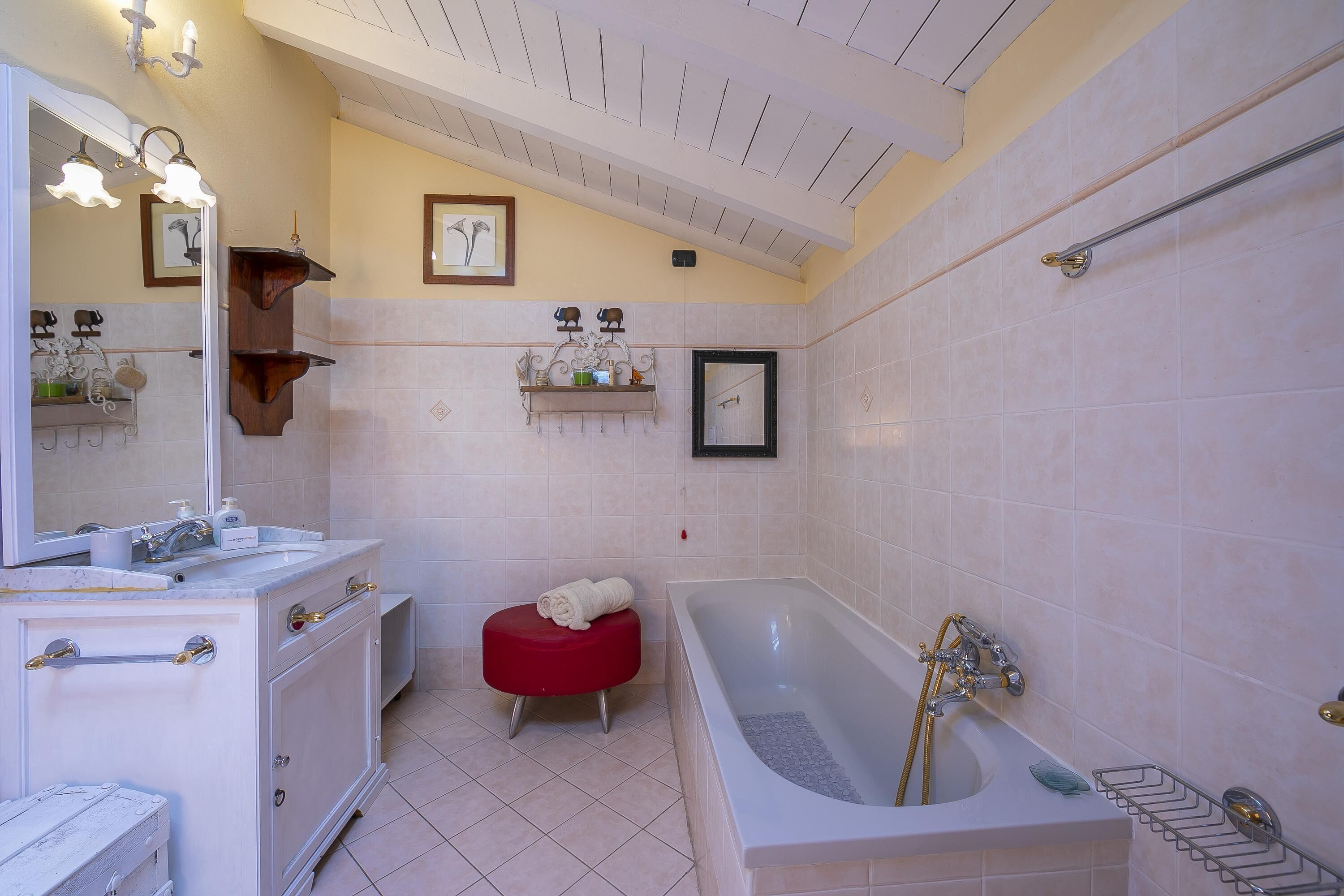 Une salle de bain avec une grande baignoire, un meuble-lavabo avec un miroir et un tabouret rouge.
