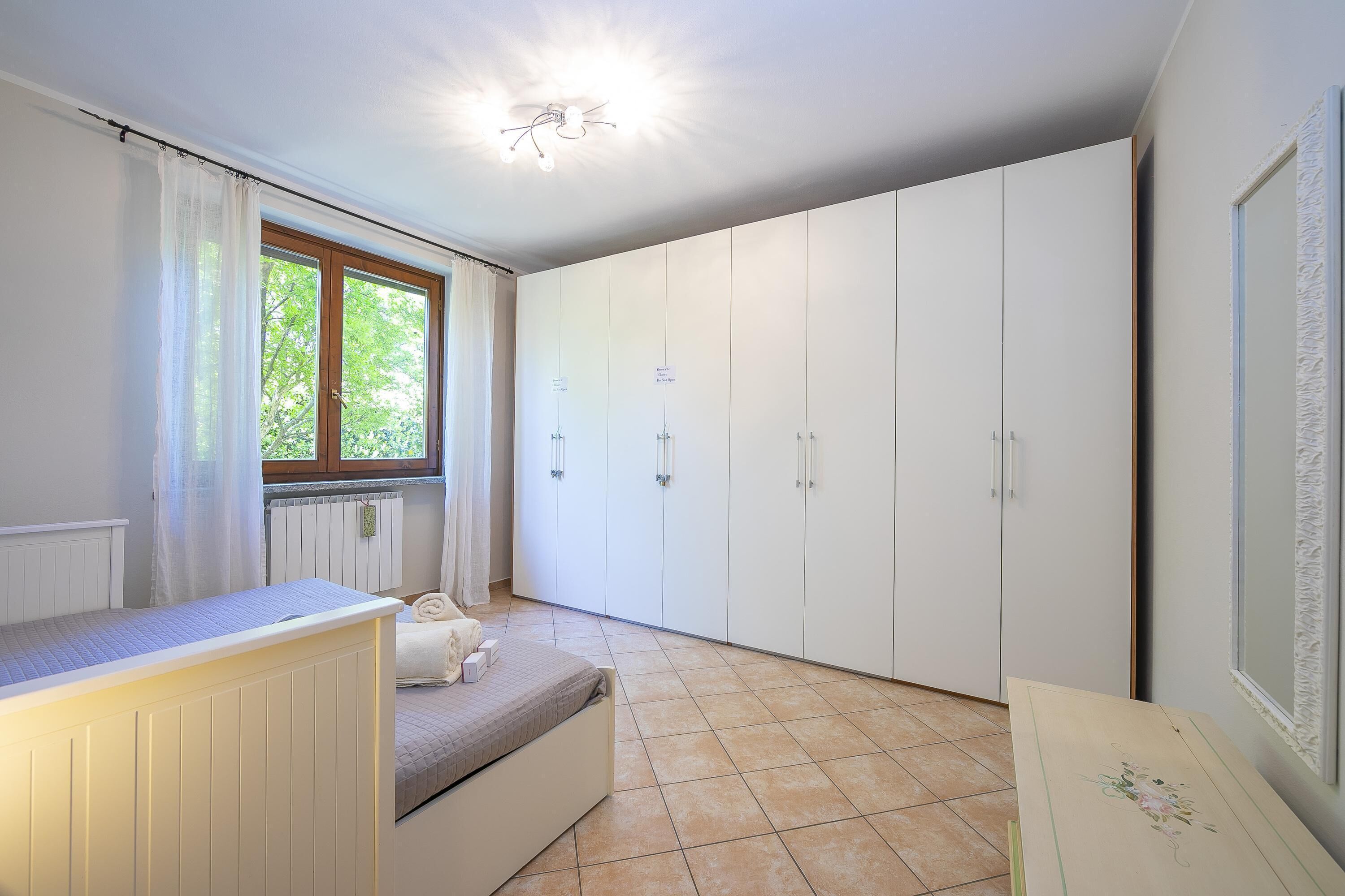 Un dormitorio con cama, ventana con cortinas, armario y radiador.