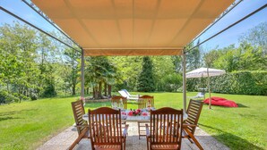 Une terrasse extérieure avec une table dressée pour quatre personnes, entourée de chaises en bois, sous une tonnelle.