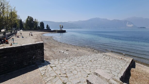 Une promenade dallée de pierres, bordant un lac paisible, avec un mur de pierre d’un côté et une rangée d’arbres de l’autre.