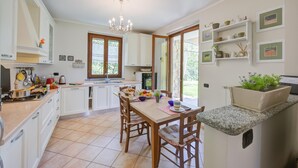 Une cuisine spacieuse avec des meubles blancs, une table à manger en bois et un îlot central intégré agrémenté d’une plante.