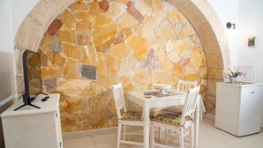 A dining area with a stone wall, white furniture, and a small refrigerator. - Nike Home 200m From Sea (Syracuse)