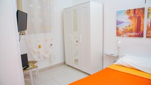 A bedroom with a bed, a wardrobe, a desk with a laptop, a TV, and a painting on the wall. - Nike Home 200m From Sea (Syracuse)