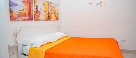 A bedroom with a bed, white headboard, and a colorful painting above it.