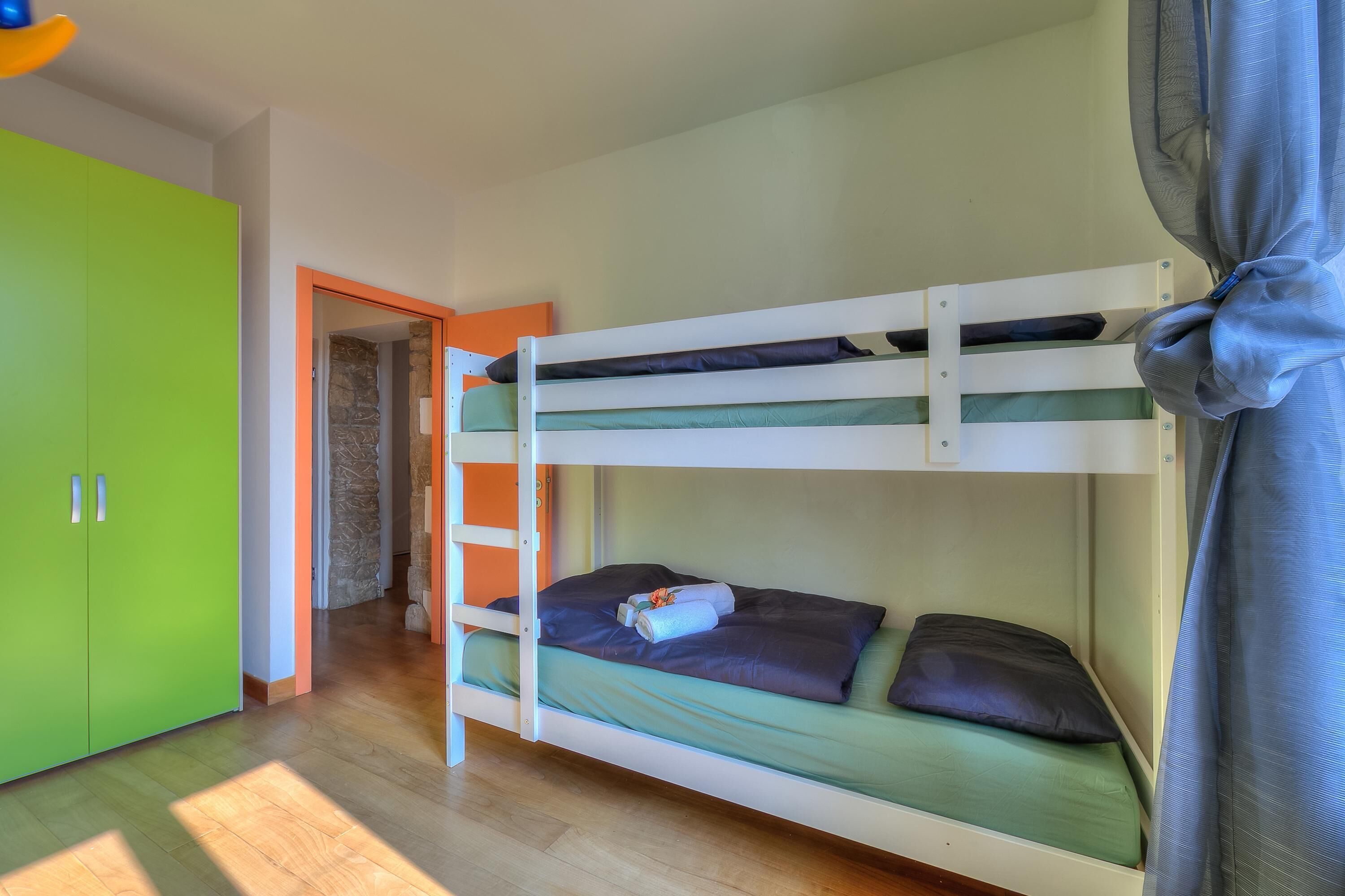 A bunk bed with a ladder, a green wardrobe, and a doorway leading to another room.