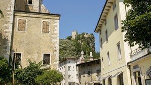 A narrow street with historic buildings, a castle on a hill, and outdoor seating areas. - Muri Di Arco in Arco (Arco)