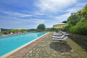 A swimming pool with lounge chairs and umbrellas, surrounded by stone walls and greenery.