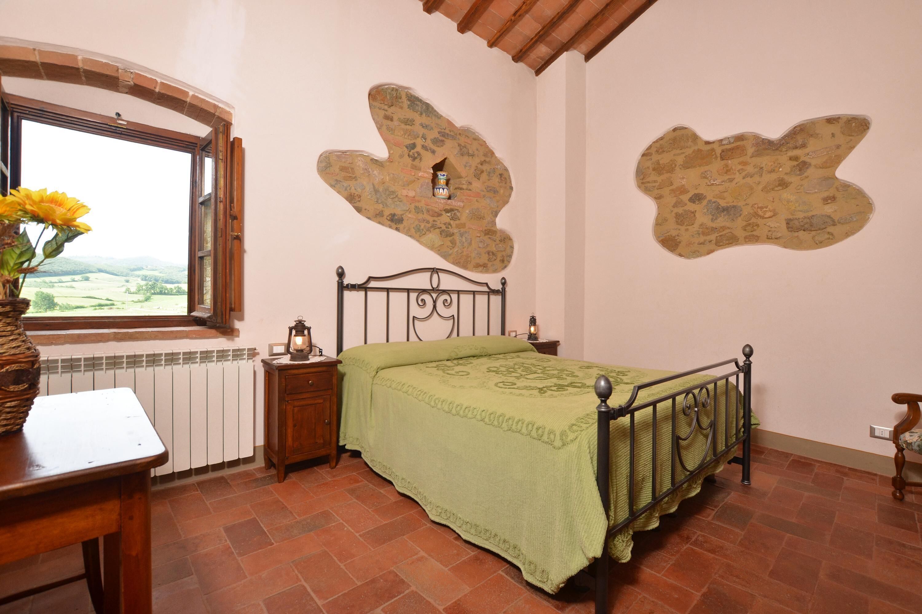 Une chambre à coucher avec un lit, une fenêtre, un radiateur, une table de chevet et un vase avec des fleurs.