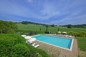 A rectangular swimming pool with a brick border, surrounded by a patio area with lounge chairs and umbrellas.