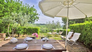An outdoor dining area with a wooden table set for two, a large umbrella, and white lounge chairs. - Pozzovecchio in Casole d Elsa (Casole d'Elsa)