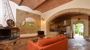 A cozy living room with a fireplace, stone walls, and an archway leading to a kitchen. - Pozzovecchio in Casole d Elsa (Casole d'Elsa)