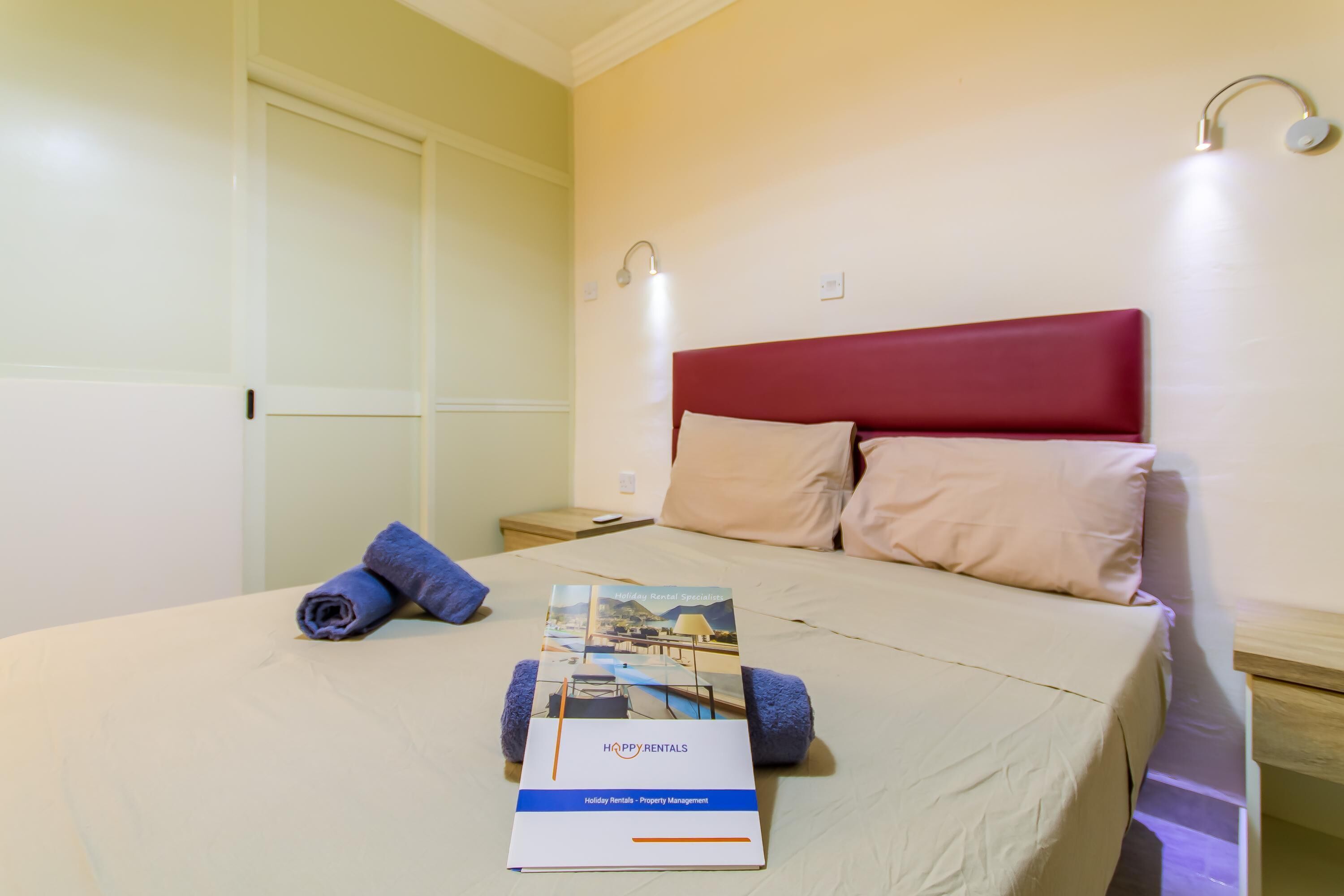 Een net opgemaakt bed met een brochure, twee kussens en een blauwe handdoek op een witte spreidek.