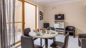 A dining area with a round table, chairs, and a television on a cabinet. - Merill Pool and Sea Charming Apart 1 (Mellieha)
