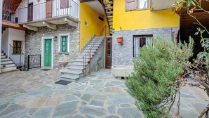 Une cour avec un sol en pierre, une porte verte, un escalier et un balcon doté d’une balustrade en bois.